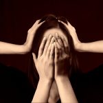 Woman closing here face with hands, and some hands around her head